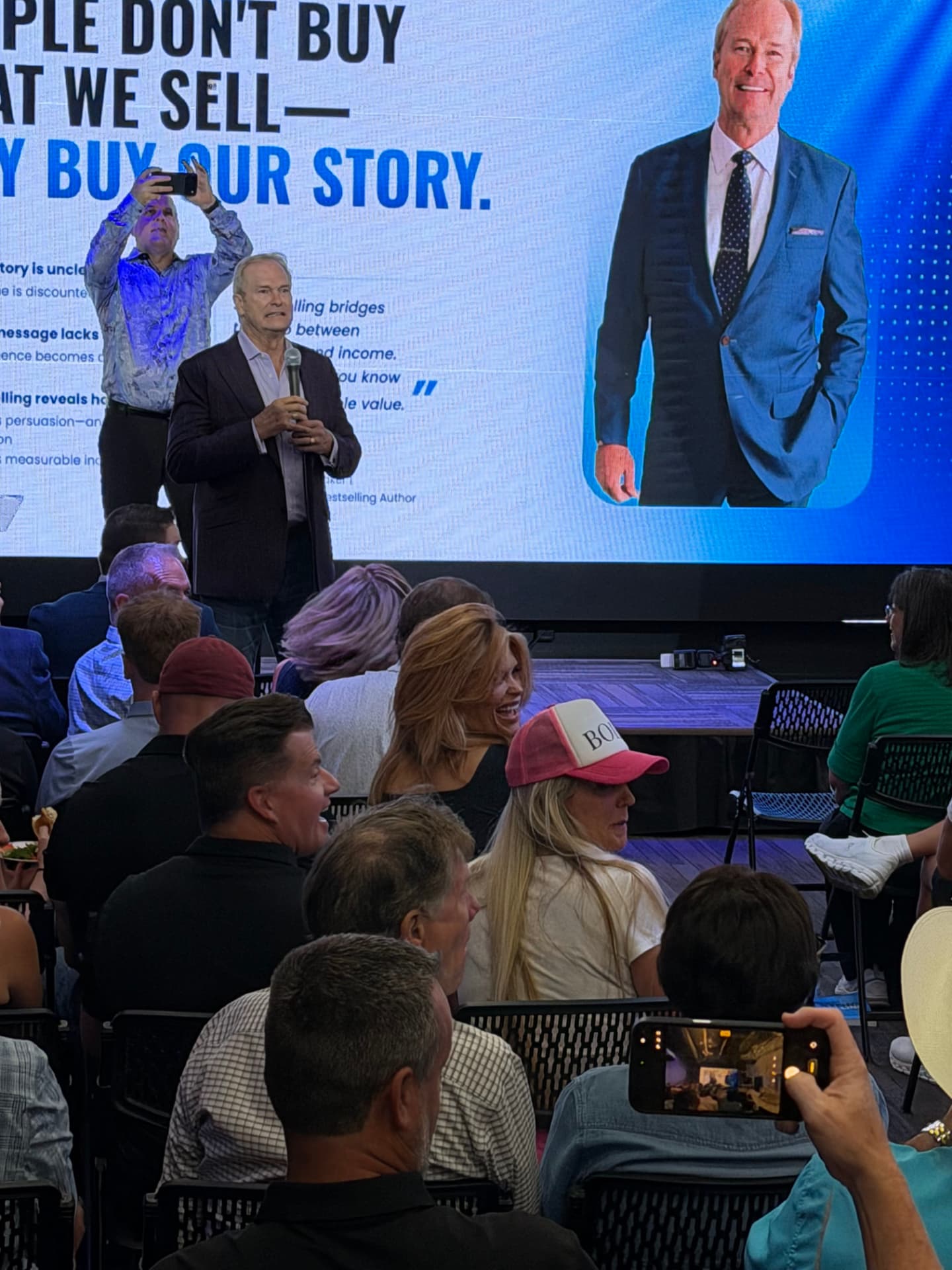 Speaker addressing the room with a microphone in front of the big screen
